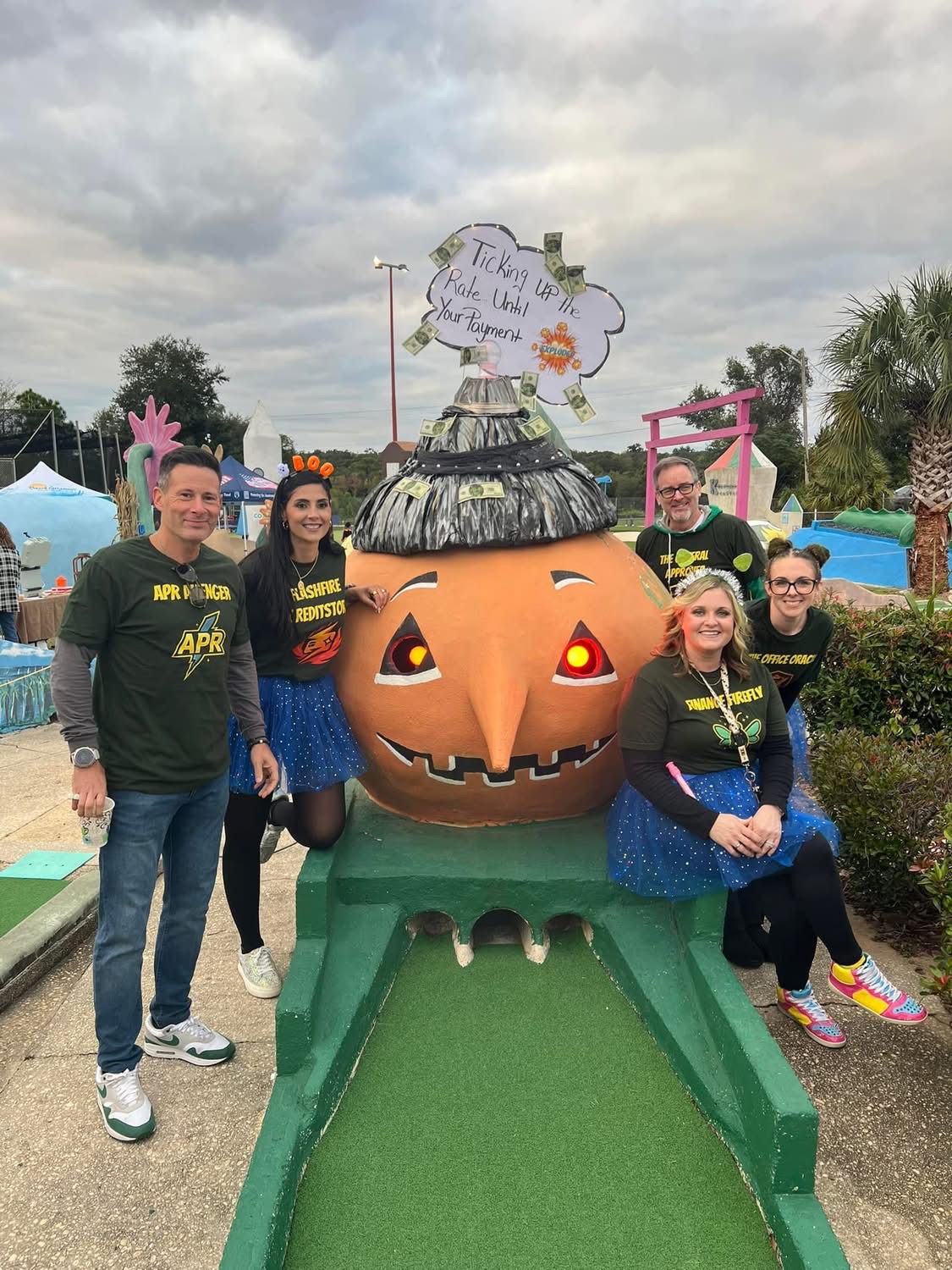 Costumed sponsor team posing with the glowing-eyed pumpkin statue on the course